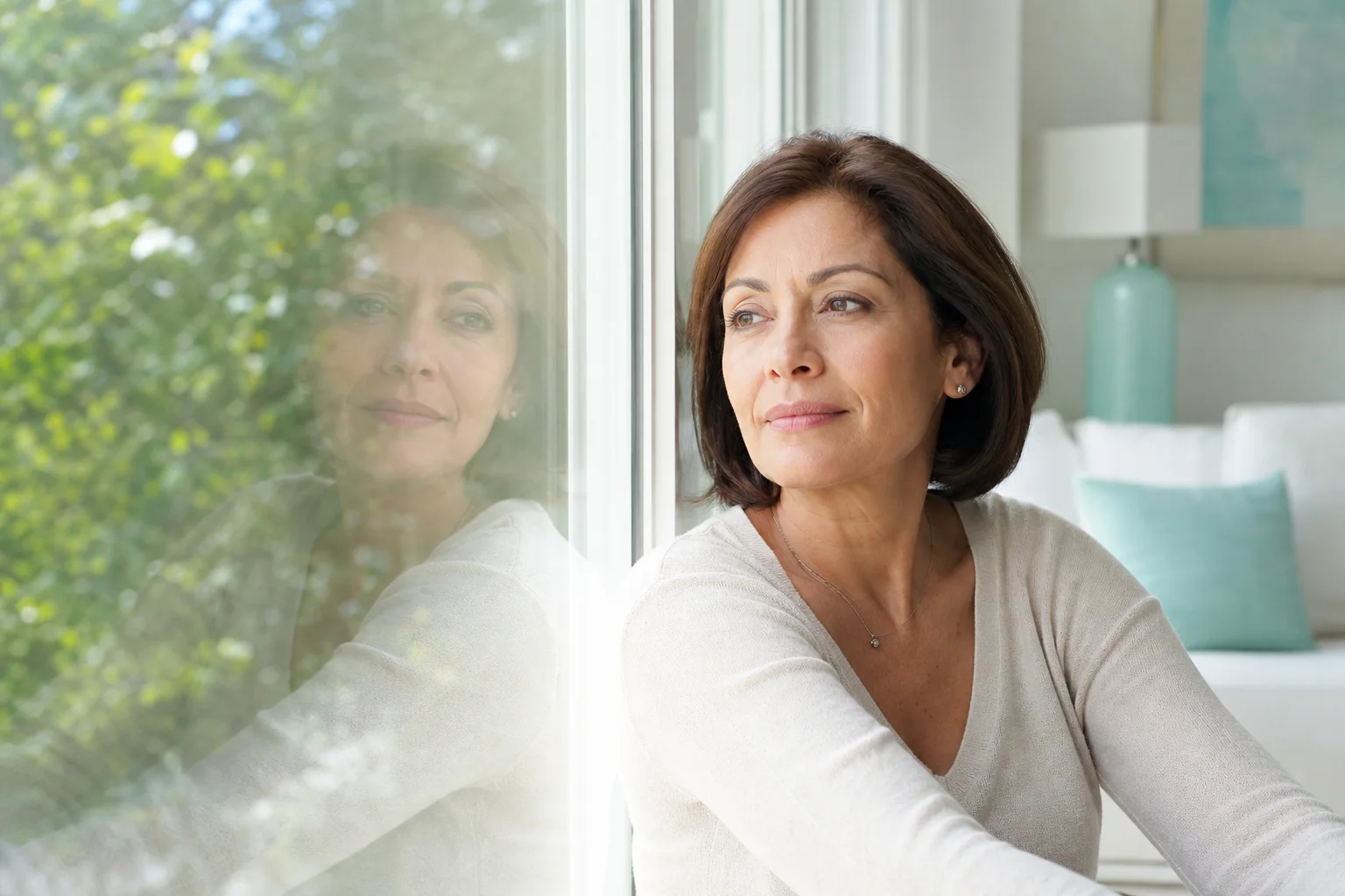 Retrato contemplativo de una mujer junto a una ventana con reflejos suaves que evocan pensamientos pasajeros